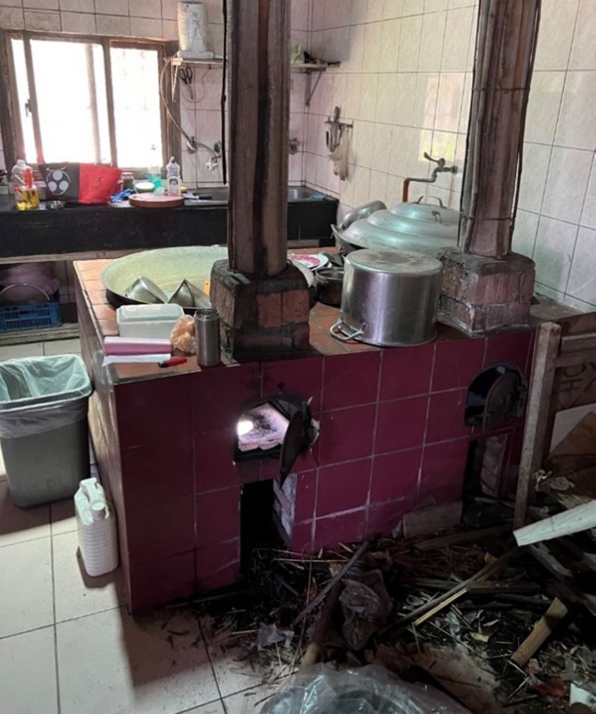  中崙村某宅灶爐。兩灶門、兩支煙囪、兩鼎鐵鍋；薪材置放於灶門前；遠處有流理台與料理台；直接用自來水供水。